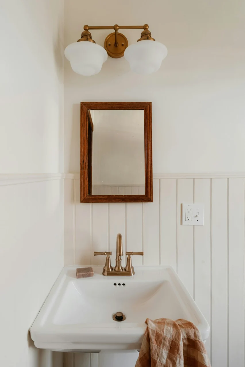 A bathroom sink with a wooden mirror and light fixture