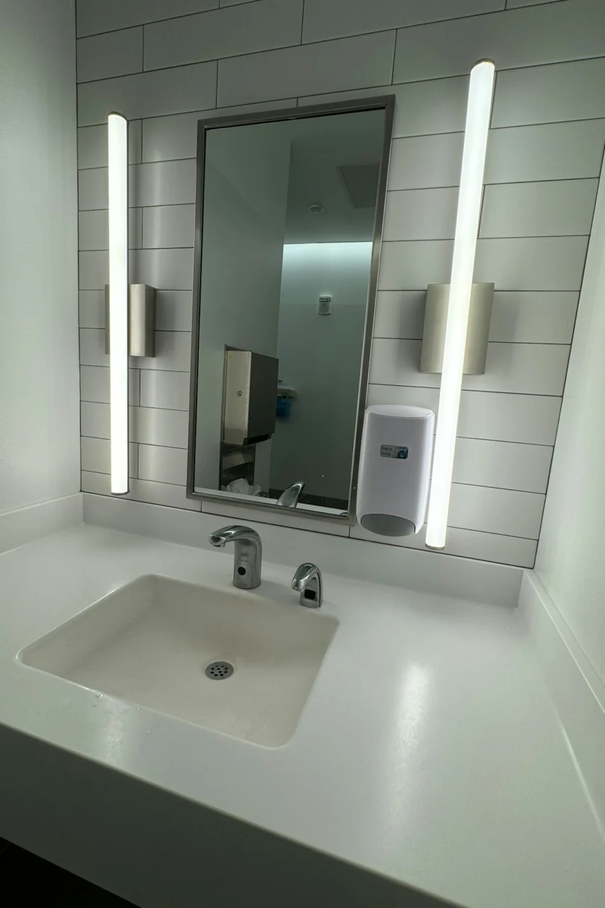 A bathroom with a sink, mirror and soap dispenser