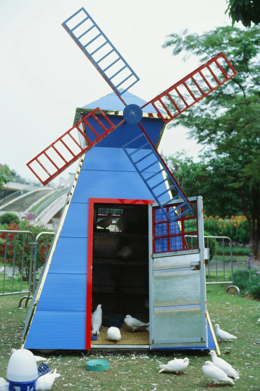 A blue windmill shaped birdhouse with white pigeons on a green lawn