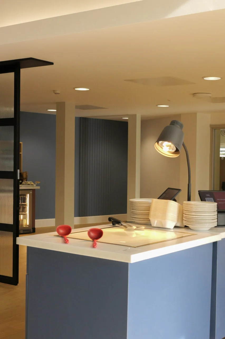 A buffet counter with stacks of plates, red ladles, and a desk lamp