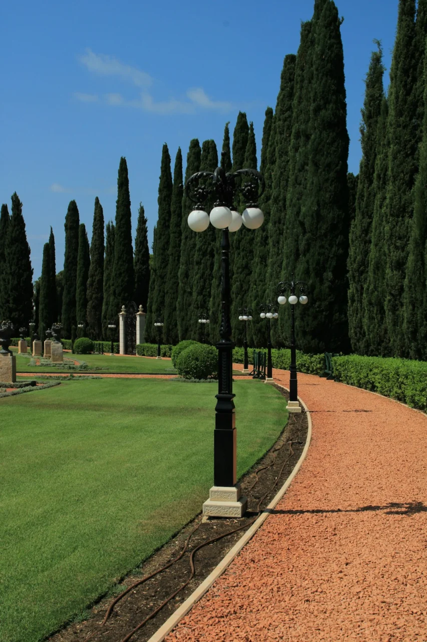 A curved gravel path lined with black lamp posts and tall cypress trees