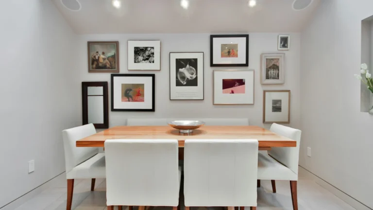a dining room table with white chairs and pictures on the wall