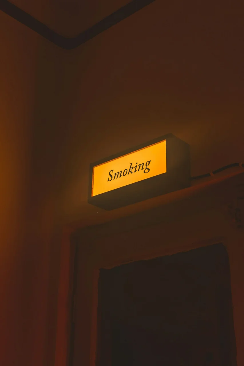 A glowing yellow sign reading "Smoking" mounted above a dark doorway