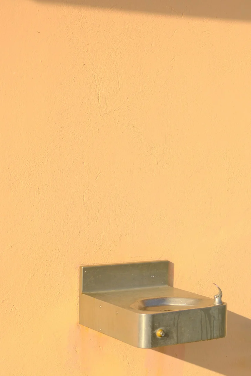 A metal drinking fountain mounted on a peach wall