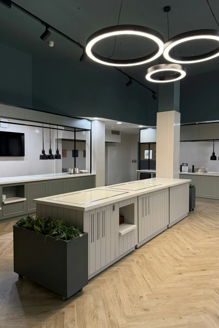 A modern kitchen with sage green cabinets, light countertops, and circular pendant lights