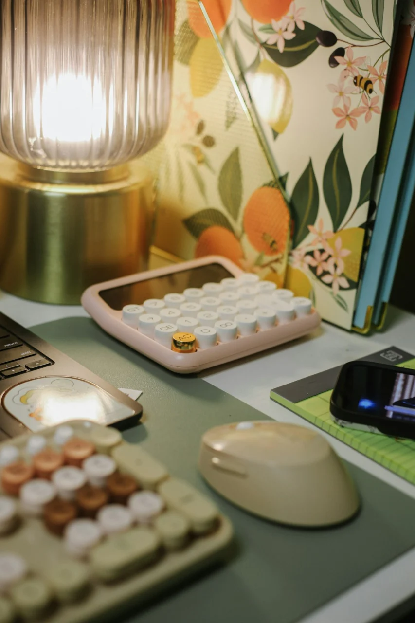 A pink calculator, a computer mouse, and a lamp on a desk workspace