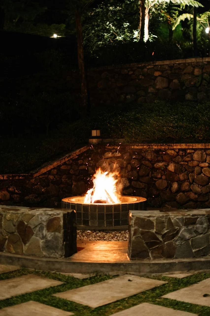 A roaring fire pit illuminates a stone wall at night