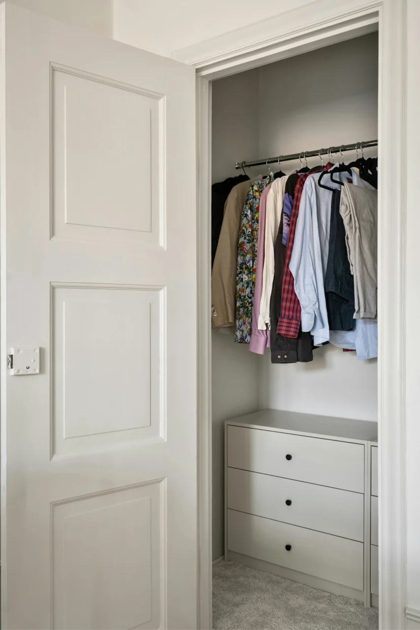 A white closet with clothes hanging on a rail
