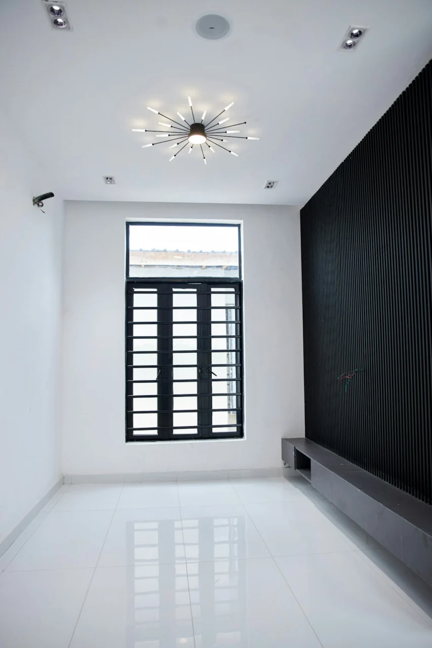 An empty room with white tiled floors, a black slatted wall, and a window