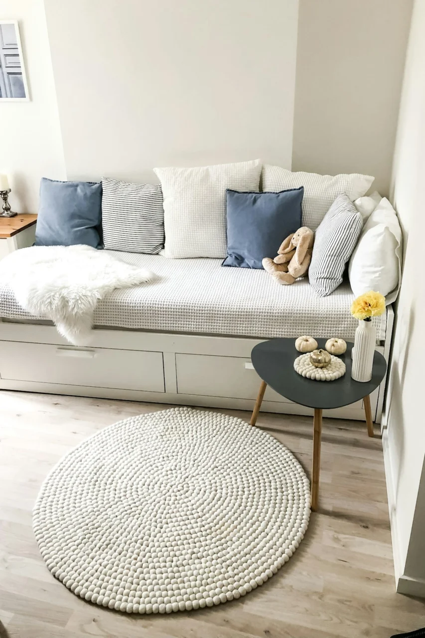 blue and white pillows on white couch and round white area mat on floor