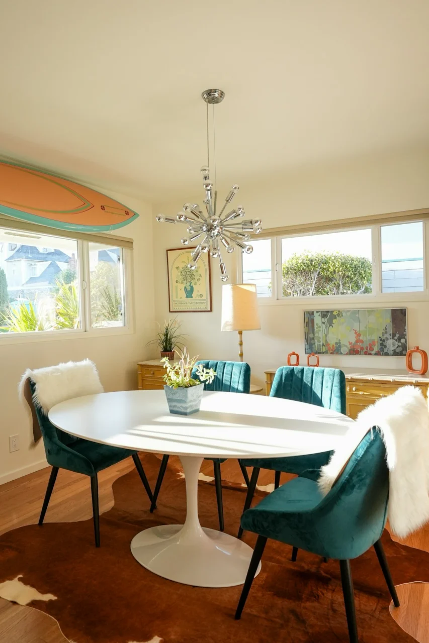 Dining room with an oval table, teal chairs, and surfboard
