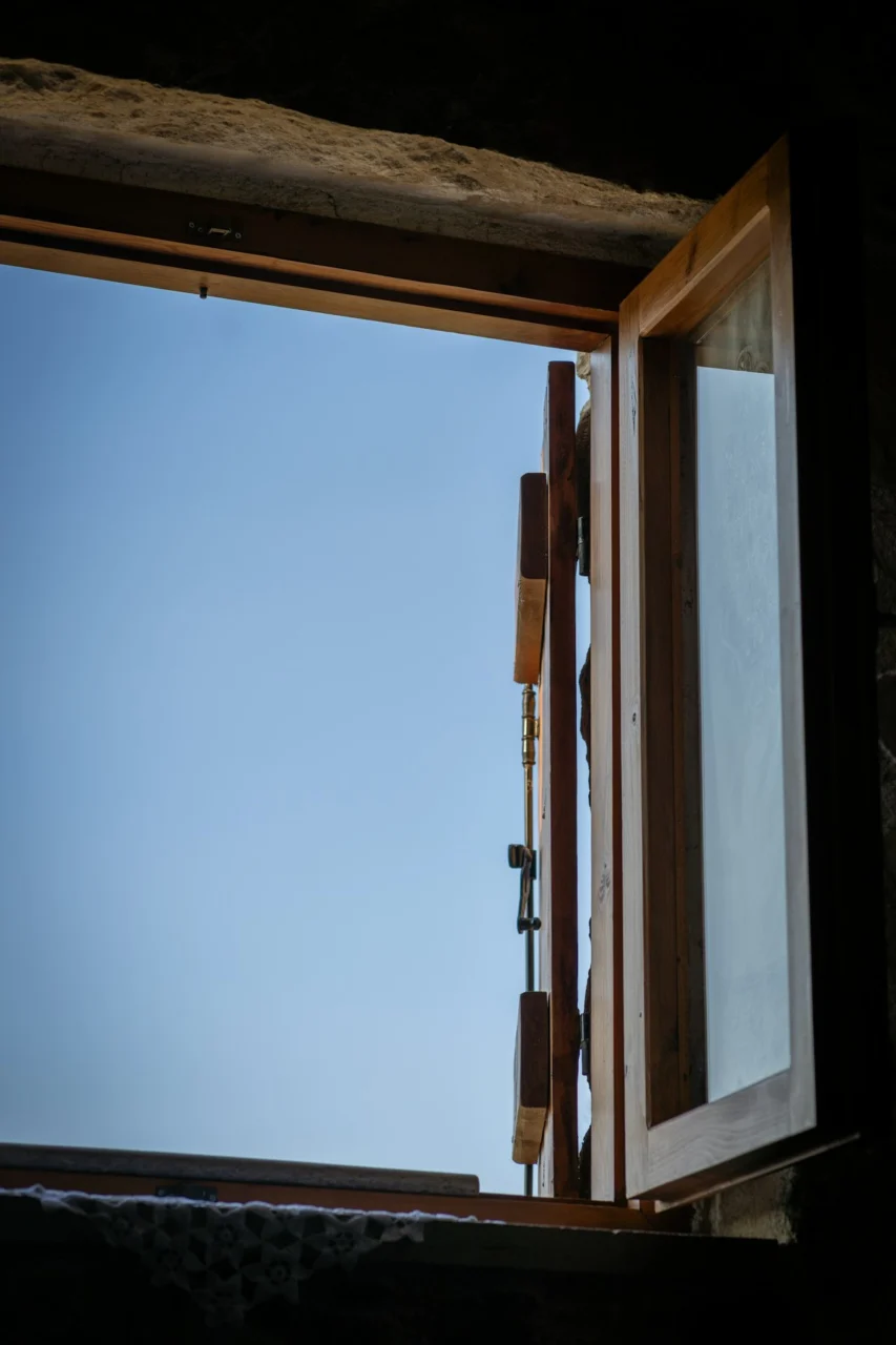 Open wooden window looking out at a clear blue sky