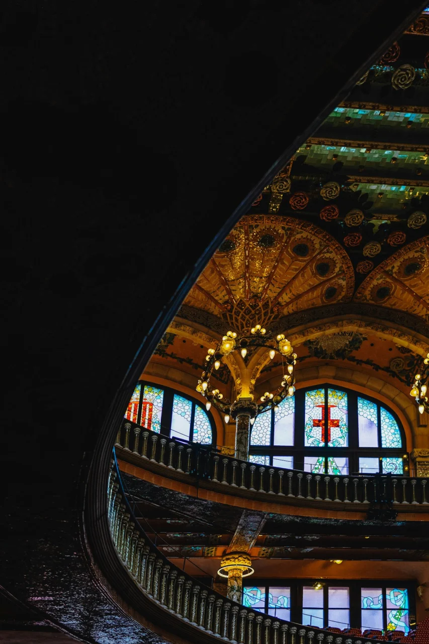 Ornate interior with chandelier, arched windows, and curved balcony