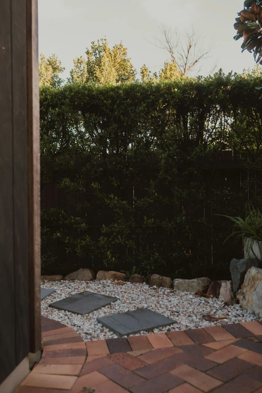 Outdoor garden space with brick path, gravel, and green hedge