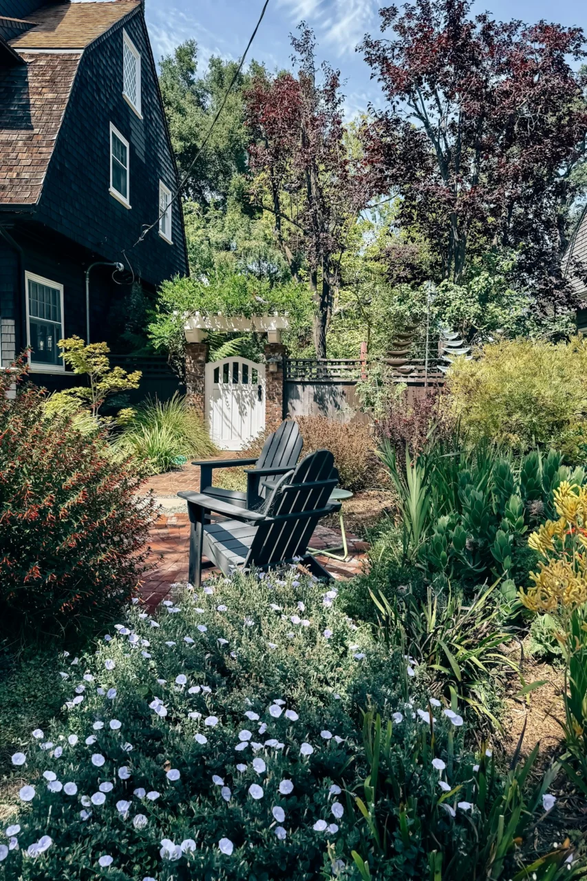 Serene garden with adirondack chairs, white gate, and lush foliage