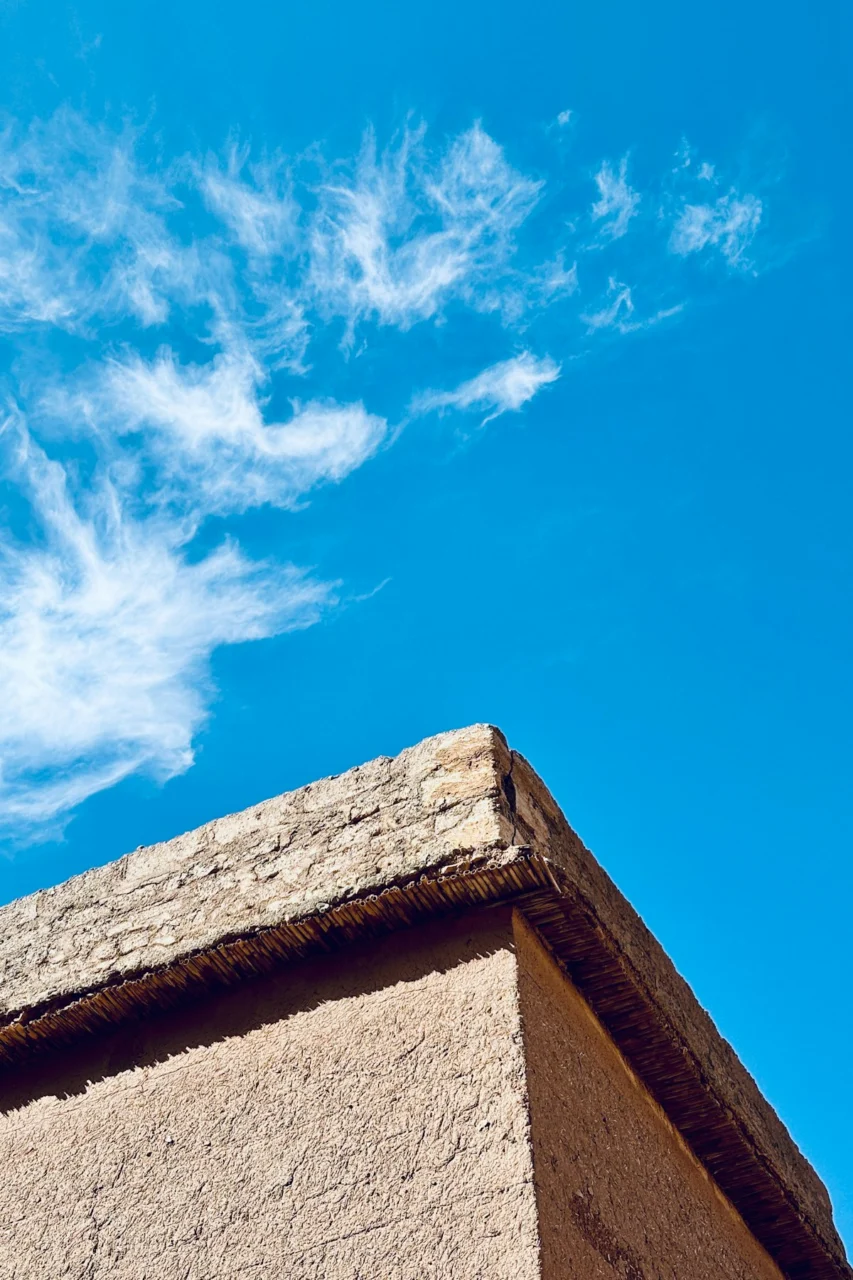 The corner of a rustic mud brick building against a bright blue sky