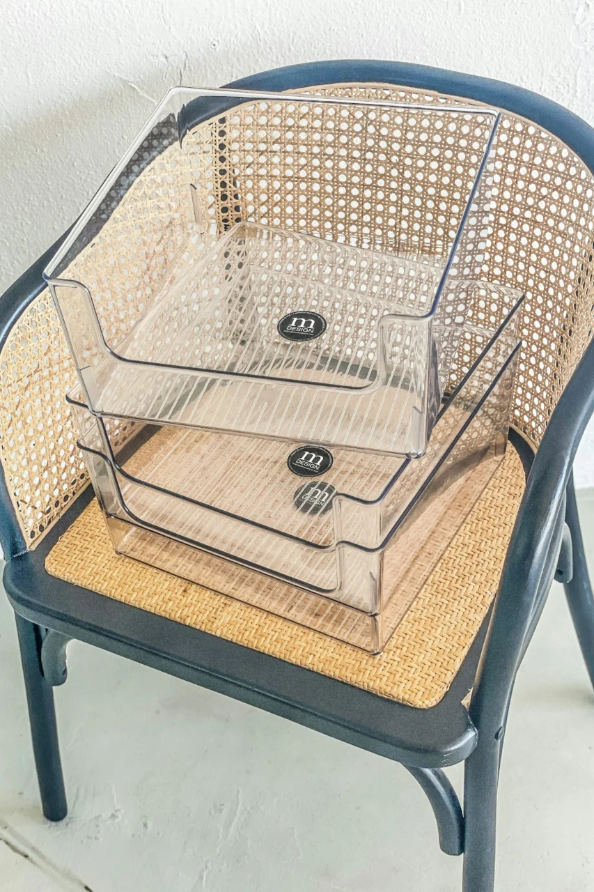 Two clear plastic organizers stacked on a dark cane chair