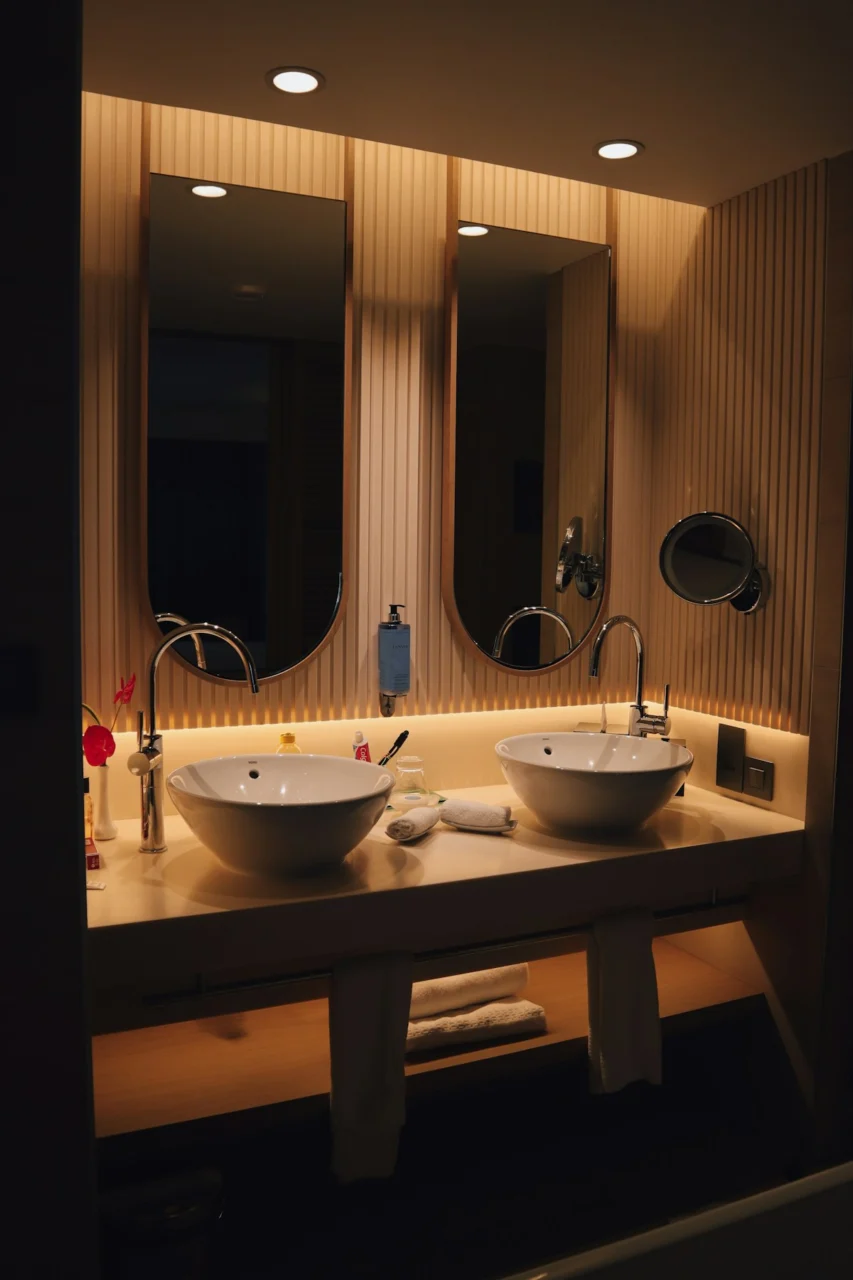Two white vessel sinks on a vanity with mirrors and warm lighting