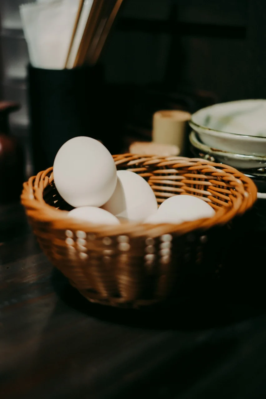 White eggs in a woven basket on a dark surface