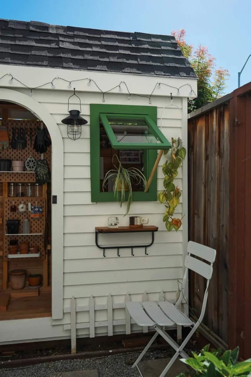 White garden shed with green window and white chair