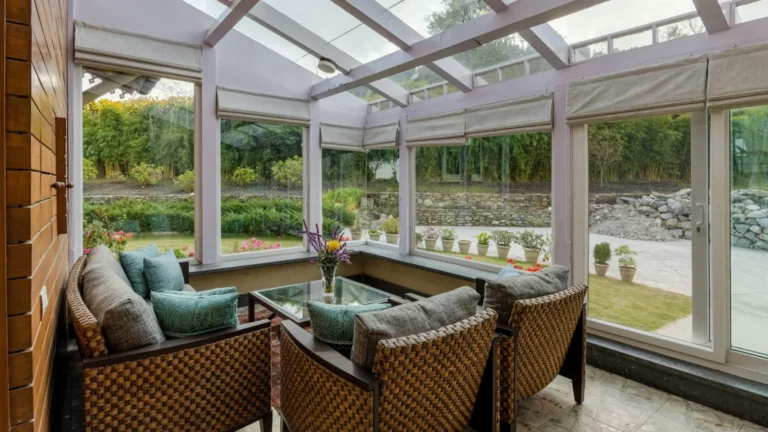 Wicker armchairs with teal cushions in a sunlit glass conservatory overlooking a garden
