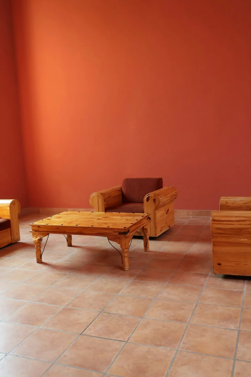 Wooden armchairs and a low coffee table on a tiled floor against orange walls
